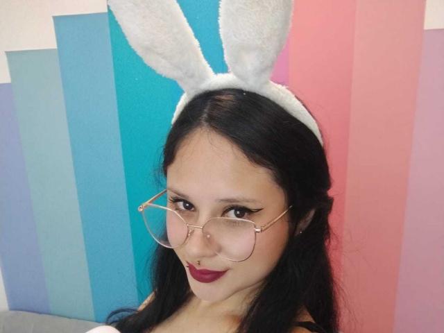 MaraVixen with black hair, white bunny ears, pink nose ring, and pink-rimmed glasses, wearing dark lipstick, smiling. Boobs not visible. Ass not visible. Pussy not visible.