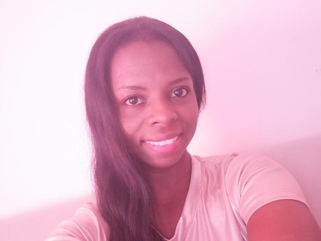 CheatingNeighbor has dark brown skin, long black hair, and is smiling with pink lipstick. She's wearing a light pink shirt and has a cute, sexy face.