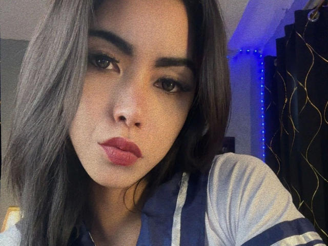 DangerousTrans69-hot with pouty lips, full eyebrows, and long dark brown hair, wearing a blue and white striped shirt, looking seductively at the camera.