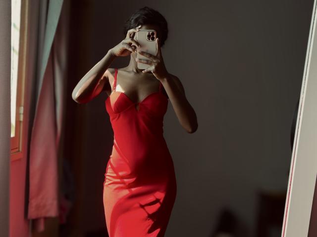 JodieFrancy in a tight, red, strapless dress, taking a mirror selfie with her phone, showing her small tits and slim ass, short black hair, in dim light.