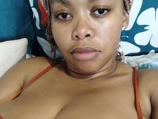 WendyStacey has medium brown skin, braided hair, and is wearing a red tank top, showing her tits and looking directly at the camera with a neutral expression.