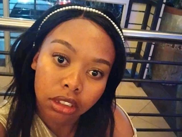 WendyStacey has dark brown skin, wide eyes, and a pearl headband. Her black hair is loose, and she's wearing a shiny top, looking slightly confused with parted lips.