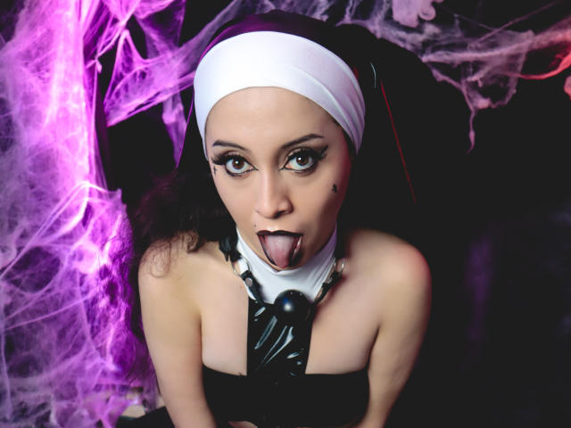 KendraSimons with a nun outfit, black latex necktie, and white headscarf, sticking her tongue out, purple smoke, and dark makeup, looking up with wide, dramatic eyes.