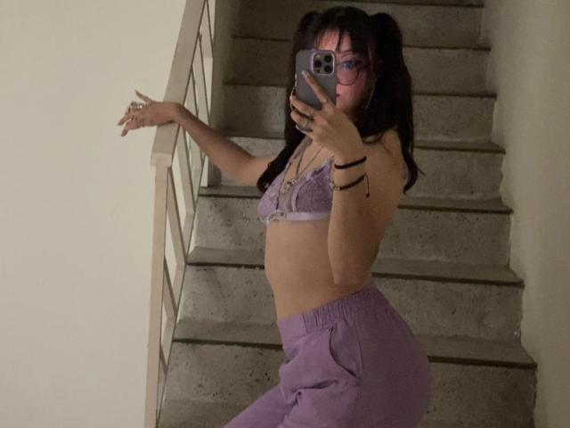 ValuuRodriguez with puffy ass, wearing purple lace bra and matching pants, taking a mirror selfie on stairs, has glasses, and pigtails, holding phone with right hand.