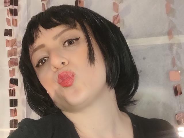 CatalinaMonyque with black bob, pouty pink lips, dark eyeliner, and a black shirt, making a kissing face. She has fair skin and a small nose.
