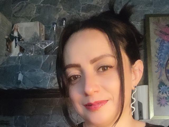 CatalinaMonyque has pale skin, brown eyes, and black hair in a messy bun. She's smiling with pink lipstick, wearing a black top and large, wavy earrings.