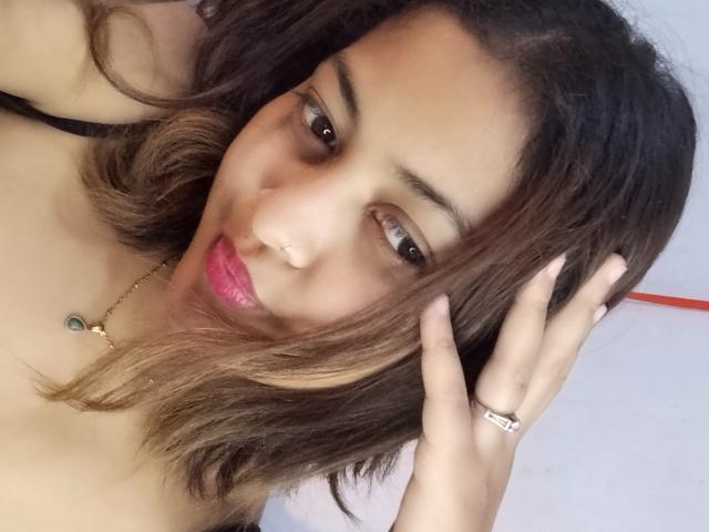 CuteCute has medium brown skin, wavy brown hair, pink lipstick, a nose ring, and a gold necklace. She's touching her hair with a ringed hand, looking at the camera.