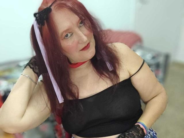 Sabrhina with red hair, black lace gloves, black strapless top, red choker, and purple ribbon, looking at camera, slightly smiling. Her tits are medium-sized, and she's wearing a bracelet.