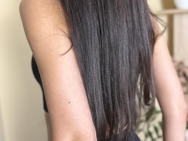 Stefanni's long, straight black hair covers her back, showing a small dark mole on her right arm, wearing a black strap, her skin is light and smooth.