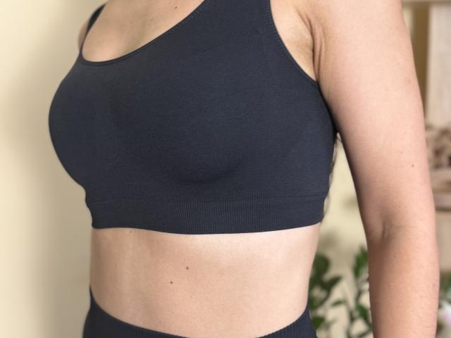Stefanni's boobs are covered in a tight, black sports bra. Her arms and midriff are visible, showing light skin and a small tan line.