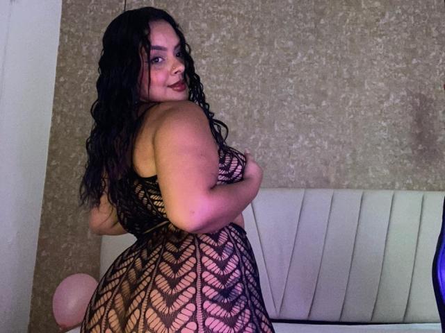 AmarantaCarey with wet black hair, wearing a black fishnet dress, showing her big ass and small tits, looking over her shoulder with a smile.