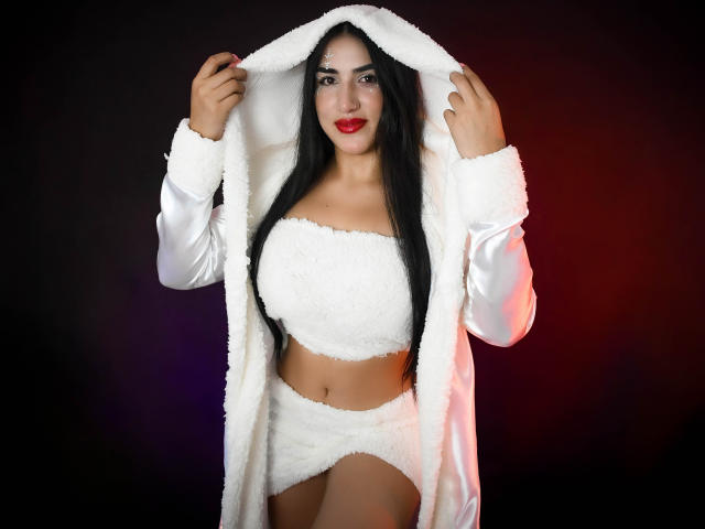 AlanaHarris with black hair, red lipstick, white fluffy robe, and matching bra-panty set, holding robe open, showing large tits, cute smile, and tan skin, standing confidently.
