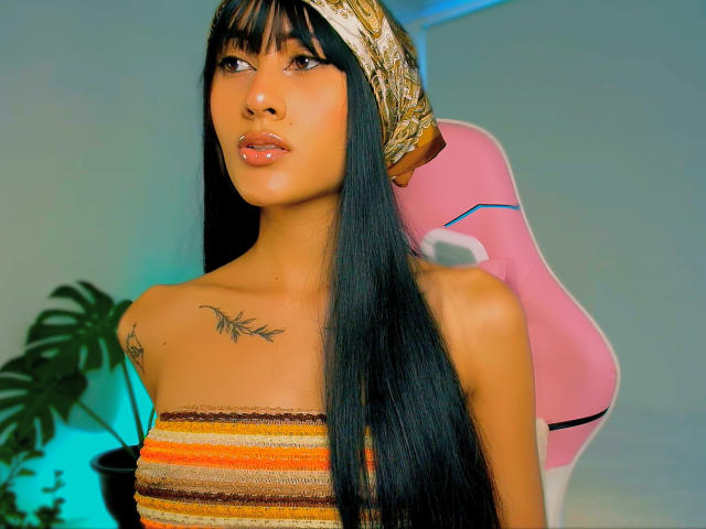 HarleyRoods with long black hair, brown eyes, and tan skin, wearing a striped top and gold headscarf, showing small tits and a tattoo on the right chest.