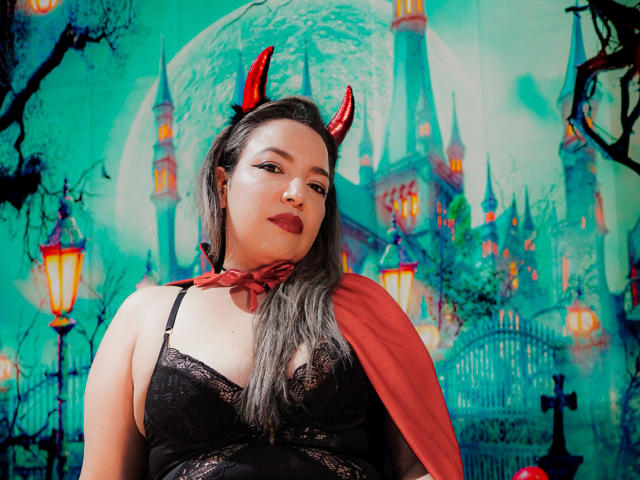 Mariehss with red devil horns, black lace bra, and red cape, dark hair, red lipstick, looking at camera, teal background, lanterns, and castle. She's a fat, sexy devil.