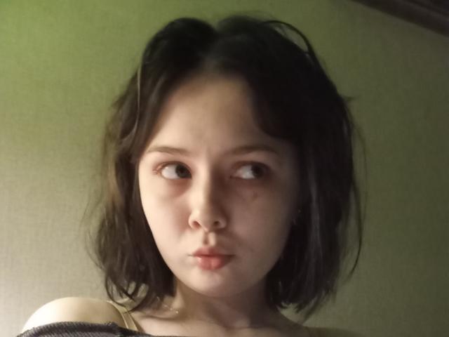 CherryDollye with short, messy dark brown hair, light skin, and pouty lips, looking to the side with a slightly confused expression, wearing a strapless top.