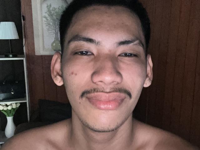HiddenDesireAru has a light brown skin tone, short black hair, thin mustache, and is shirtless with a slight smirk, showing a small facial mole on the left side.