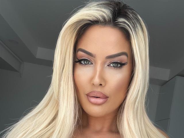 BlancheSummer has blonde hair, green eyes, full lips, and thick eyebrows. Her makeup includes long, dramatic eyelashes. She's looking directly at the camera with a neutral expression.