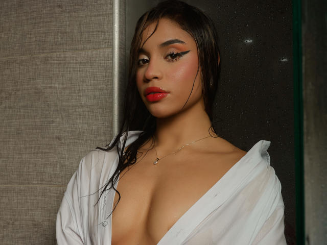 LunaVali with wet black hair, red lipstick, and winged eyeliner, wearing a white, open shirt revealing her tits. She has a necklace and a subtle, sexy look.