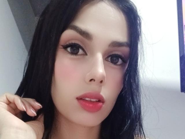 AnaisHilton has long black hair, pinkish-red lips, and dark eyebrows. Her eyes are half-open with long eyelashes. She's looking at the camera with a slightly parted mouth.