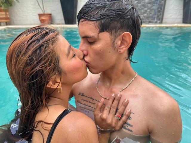 DannaXFabian and a dude kissing in a pool, both wet with water on their chests. Dude's got tattoos and a gold chain, DannaXFabian's got brown hair and a ring.