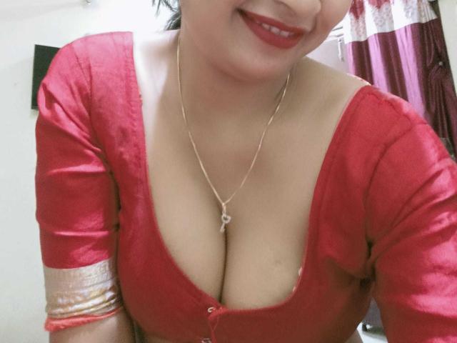 ElizaNdKeo69 has big, shiny red tits in a low-cut top, wearing a gold necklace with a small heart, smiling with red lipstick, and has light skin.