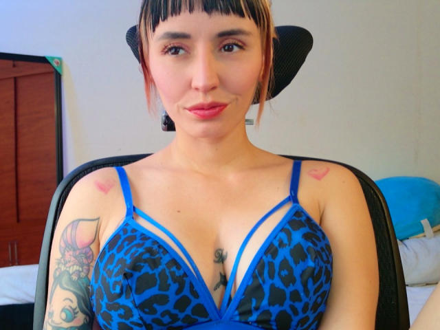 SaraleePoison is on all fours, wearing a white shirt, with her bare ass and pink pussy prominently displayed in the center of the image. Her tattoo is visible.