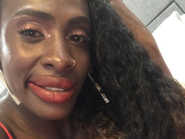 SamaraaJackson69 has dark brown skin, long curly black hair, red lipstick, and is sticking out her tongue with shiny eyes, wearing a nose ring and gold earrings.