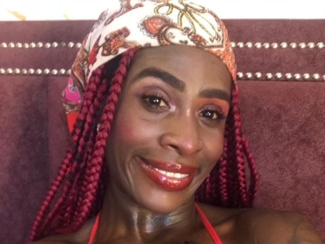 SamaraaJackson69 with dark brown skin, red braids, paisley headwrap, red lipstick, and a smile, showing off shiny lips and tattooed neck, looking cute and happy.