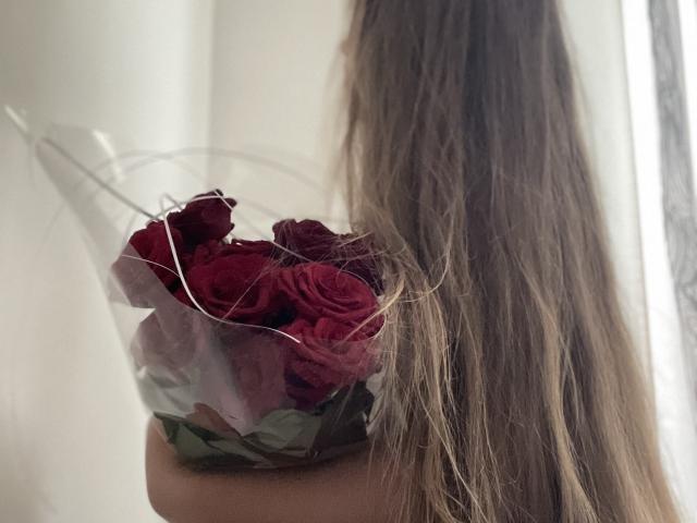  Dooris holding a bouquet of red roses with a clear plastic wrap and white string, long brown hair covering the right side of her face.