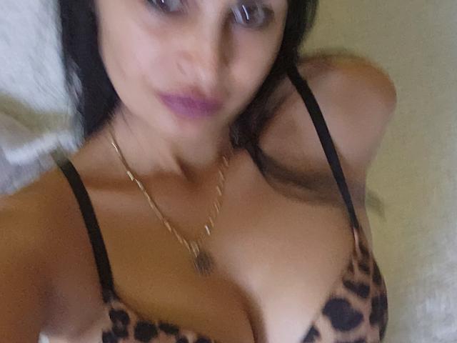 TheSunshine has tan skin, dark hair, purple lipstick, and wears a leopard print bra, showing her big tits with black straps and a gold necklace.