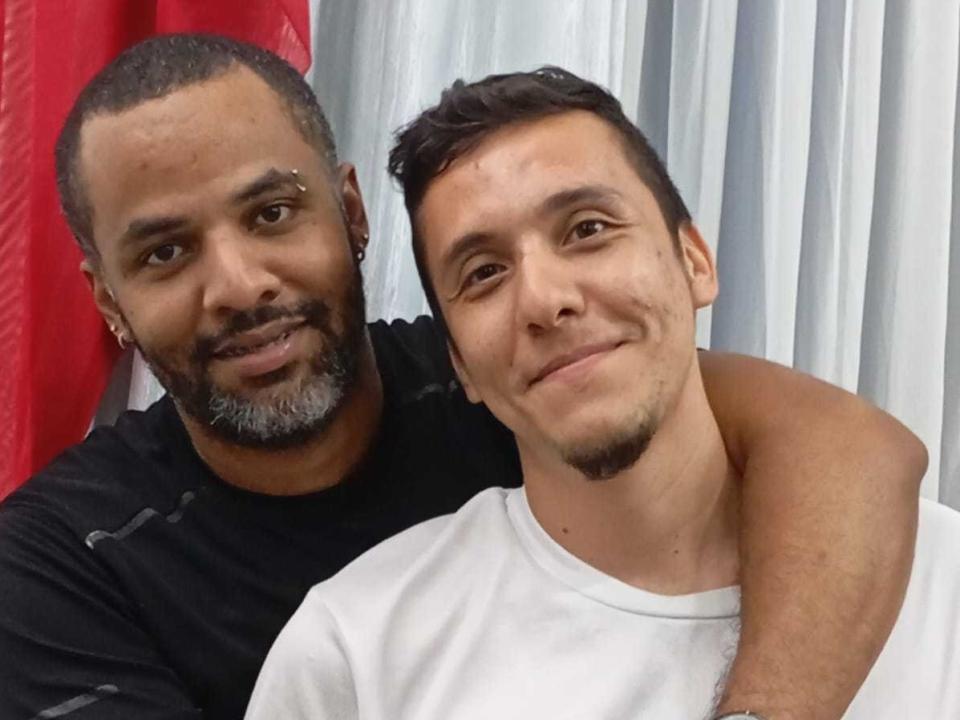 MatheoVictor with a beard and black shirt has his arm around MatheoVictor with short brown hair and white shirt, both smiling. MatheoVictor's arm is around MatheoVictor's neck.