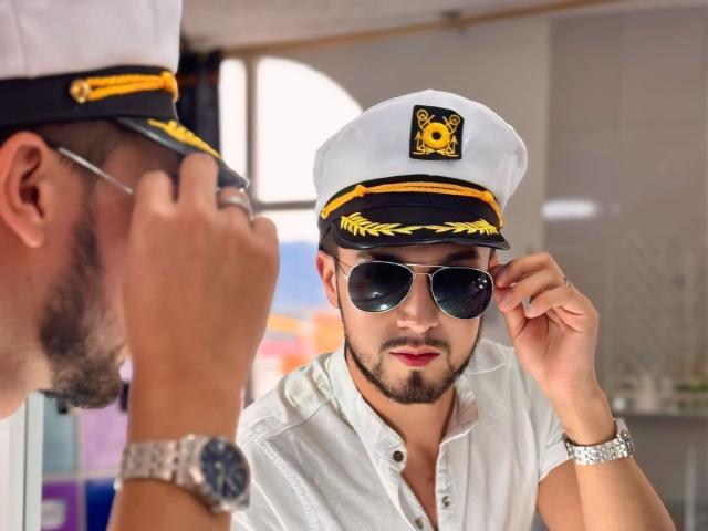 DaltonWhite, com um chapéu branco de capitão, óculos de sol pretos e uma camisa branca, ajustando o chapéu. Outro DaltonWhite, com um chapéu e óculos semelhantes, em primeiro plano..