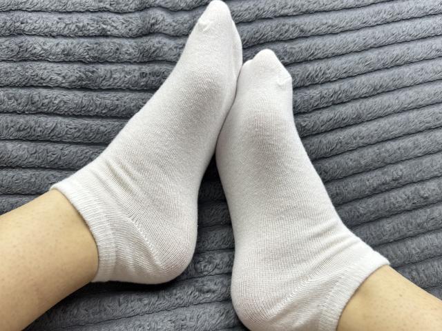 Los calcetines blancos de SophieAndWhtney, con puntas afiladas y ligeramente arrugados, están sobre una superficie gris, con relieve y textura. Los calcetines cubren los pies y los tobillos de SophieAndWhtney..