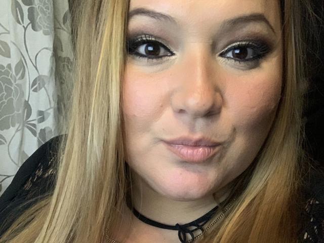 LaVa24-hot a les cheveux blonds, les yeux marrons avec un trait d'eye-liner noir, et elle poute ses lèvres roses. Elle porte un haut en dentelle noire et un collier en dentelle noir..