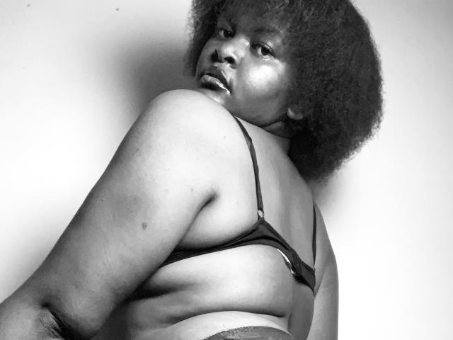 SpiceBomb with dark skin and afro, wearing a black bra, looking back, showing her back, big ass, and slightly visible tits. Black and white, sexy, confident.