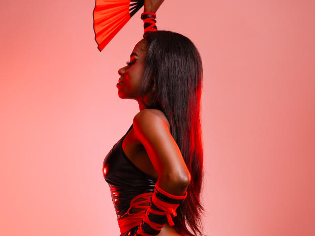 MiaHopson with dark skin, long straight black hair, wearing a black top, red rope binding, holding a red fan, red light highlighting her profile, side view, profile shot.