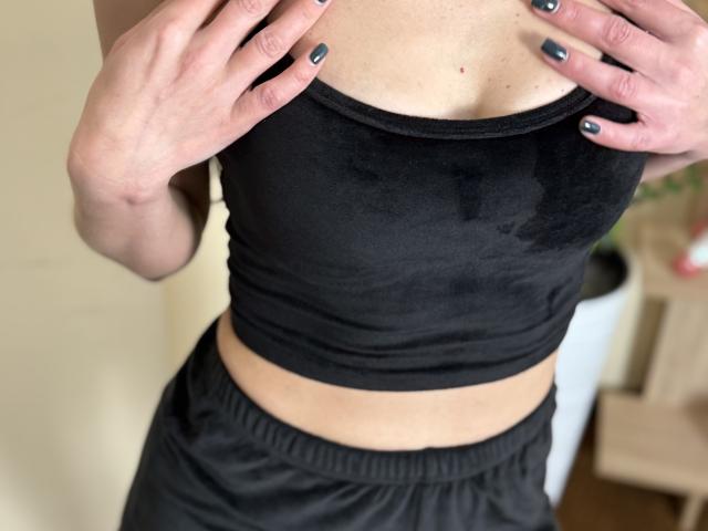 Il reggiseno sportivo nero di Stefanni, leggermente bagnato, con piccole macchie d'acqua, con le mani sul petto, unghie dipinte di grigio scuro, indossa pantaloni neri, luce morbida di metà giornata, texture della pelle delicata..