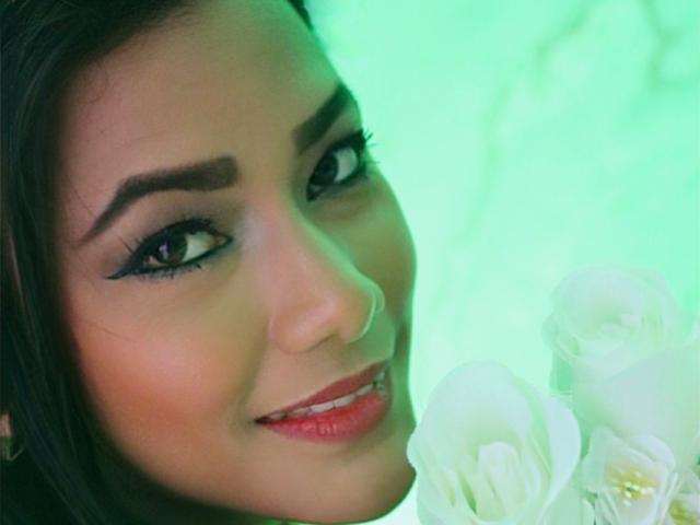 KarlaSould's face with dark eyebrows, long eyelashes, red lipstick, and a smile, holding white flowers, green light effect. Boobs not visible, focus on face and flowers.