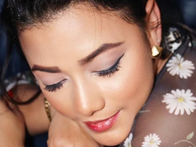 KarlaSould has a pretty face with dark eyes, heavy eyelashes, and pink lipstick. She's wearing a floral sheer top, gold earrings, and has her head down, smiling softly.