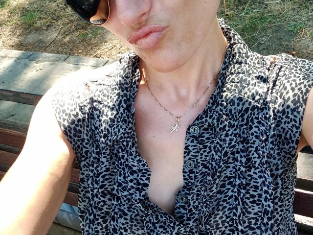 BellaJulls with pouty lips, wearing a leopard print shirt, buttoned down, showing a hint of cleavage, and a small "P" necklace, with black sunglasses.