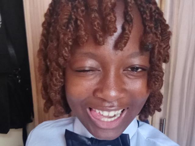 NataWilma with dark brown curly hair, one eye closed, smiling with white teeth, wearing a blue bowtie, looking cute and happy.