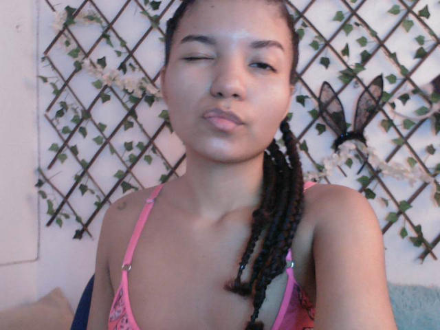 SexyLaddy with medium brown skin and braided hair, wearing a pink lace top, winking and making a pouty face, showing small tits and a cute nose.