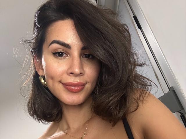 LadyDarkEyes ha capelli castano chiaro ondulati, sopracciglia scure, eyeliner e un sorriso appena accennato. Indossa orecchini dorati e un top nero con spalline, e ha una carnagione chiara..