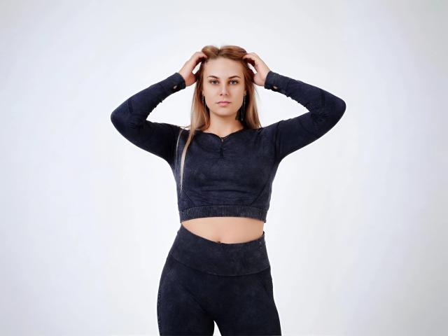NabaPretty has a serious face, hands in her long brown hair, wearing a dark blue, long-sleeve, crop-top and matching high-waist, black, leggings.