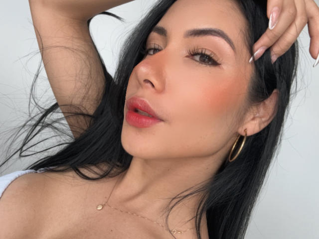 ArianaRogers has long black hair, golden hoop earrings, and is winking with her hand in her hair. She has pink lips, tan skin, and a subtle makeup look.