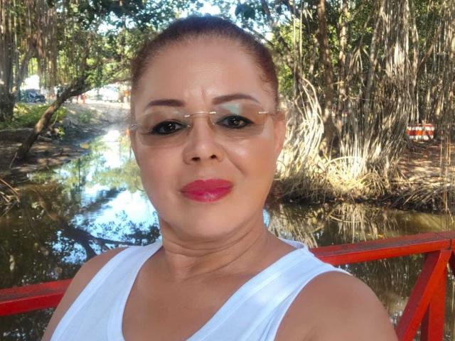 HornyFemme69 has tan skin, red lipstick, and glasses, with her brown hair in a bun. She's wearing a white tank top, and has a small, cute butt.