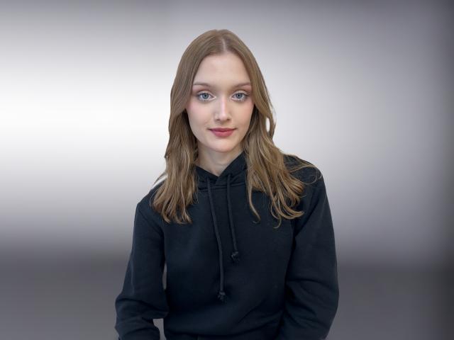 AliceAdamsy with straight brown hair, blue eyes, and black hoodie, looking slightly to the left, smiling softly. Her tits are small, and she has a cute face.