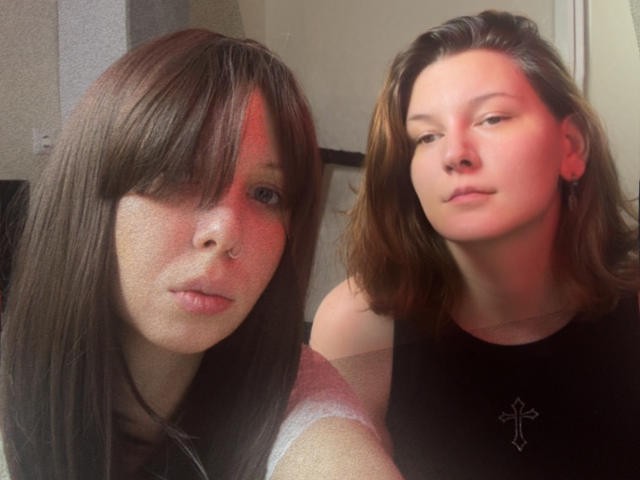 SophieAndWhtney with brown hair and freckles on left, red skin, nose ring, and subtle smile. Whtney with brown hair, black top, cross necklace, and serious expression.