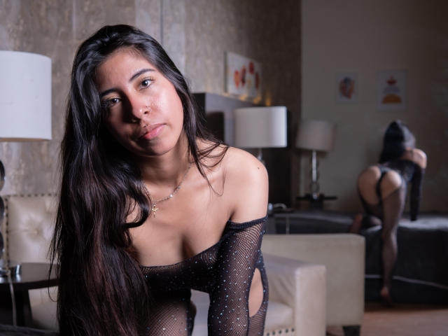 LinaSpearce with long black hair, wearing a sheer black mesh top, exposing her small tits and nipples. Her ass is in the mirror, wearing black lingerie.