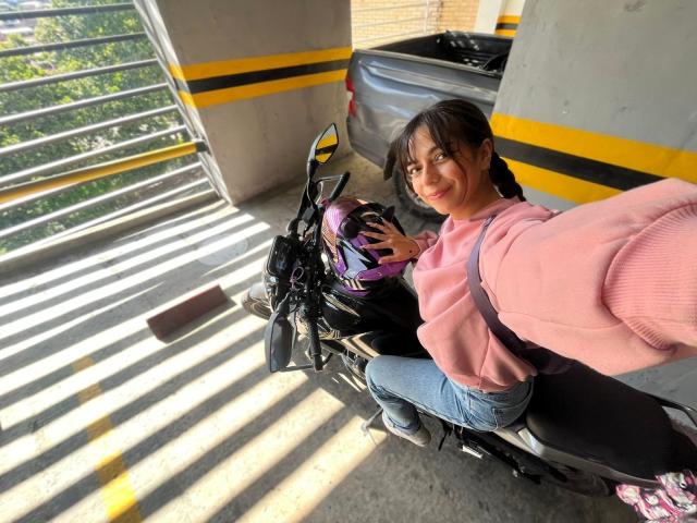 SamantaCarter, pink hoodie, blue jeans, black motorcycle, purple helmet, holding it, smiling, parking lot, sunlight, stripes on ground, SamantaCarter's ass slightly visible, black motorcycle seat.